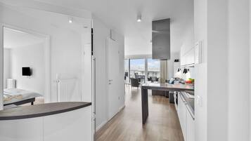 A modern kitchen with white cabinetry, a central island, and a view to the living area.