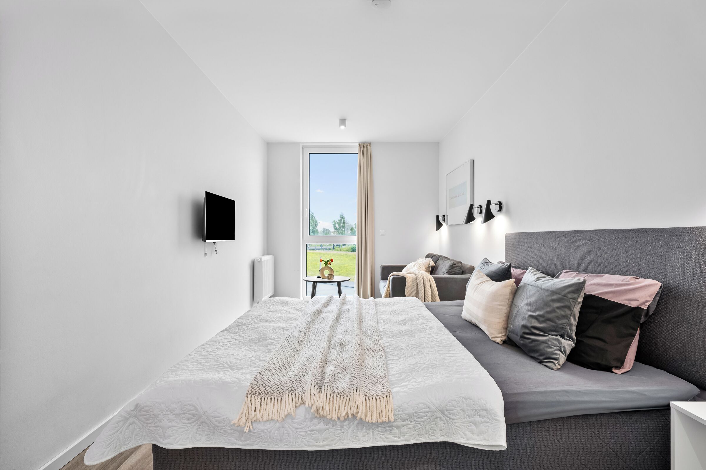 A modern bedroom with a large bed, a sofa, a TV, and a window with a view.