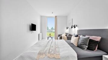 A modern bedroom with a large bed, a sofa, a TV, and a window with a view.
