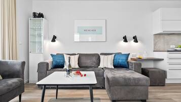 A modern living room with a grey sofa, a white coffee table, and a kitchen area in the background.