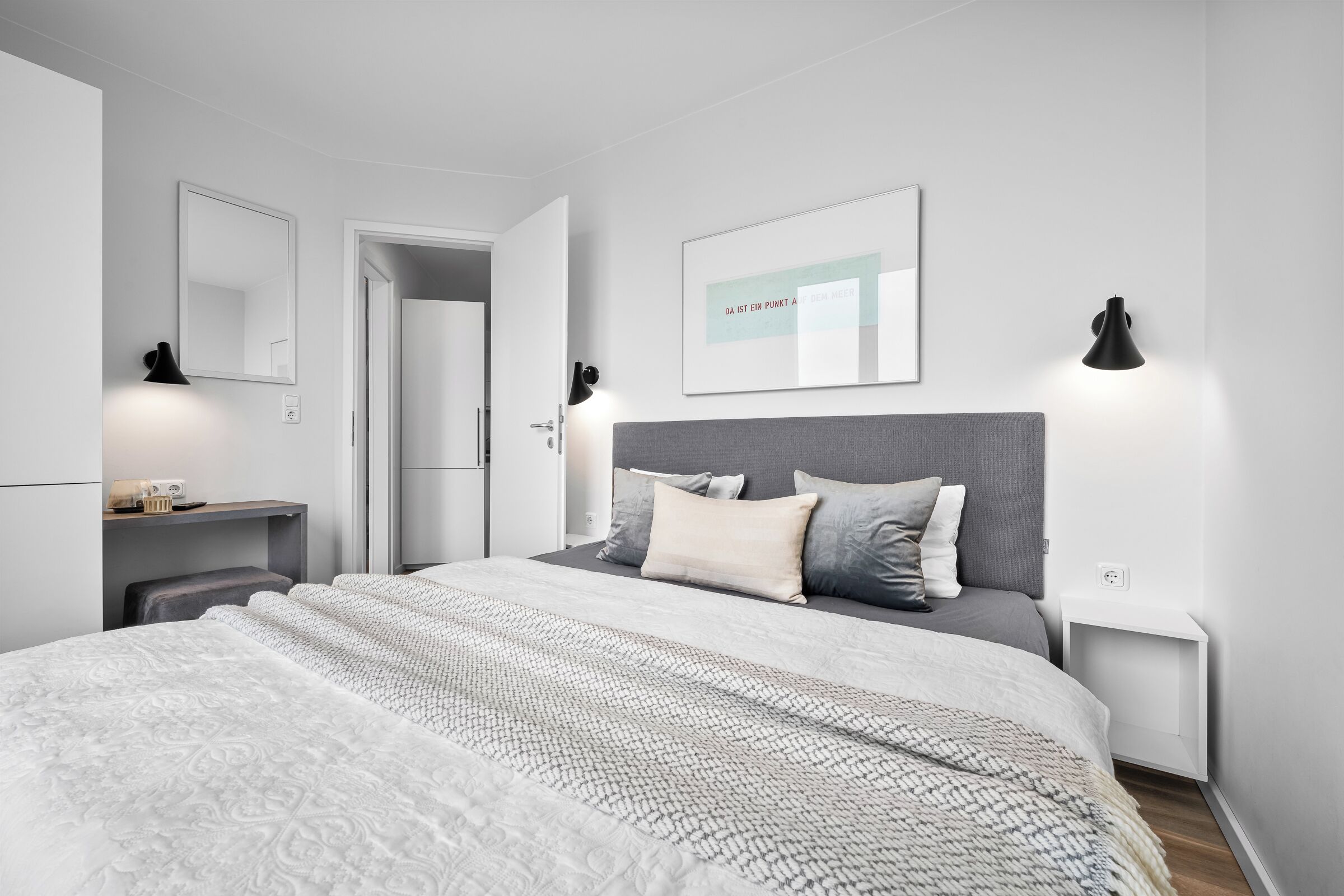 A modern bedroom with a large bed, bedside tables, a mirror, and a framed quote on the wall.