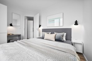 Een moderne slaapkamer met een groot bed, nachtkastjes, een spiegel en een ingelijst citaat aan de muur.
