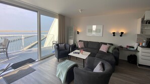 Ein modernes Wohnzimmer mit Sofa, Sesseln, einem Couchtisch und Meerblick durch eine große Schiebetür.