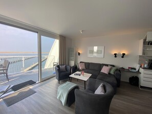 Una sala de estar moderna con un sofá, sillas, una mesita de centro y vistas al mar a través de un gran ventanal corredero.
