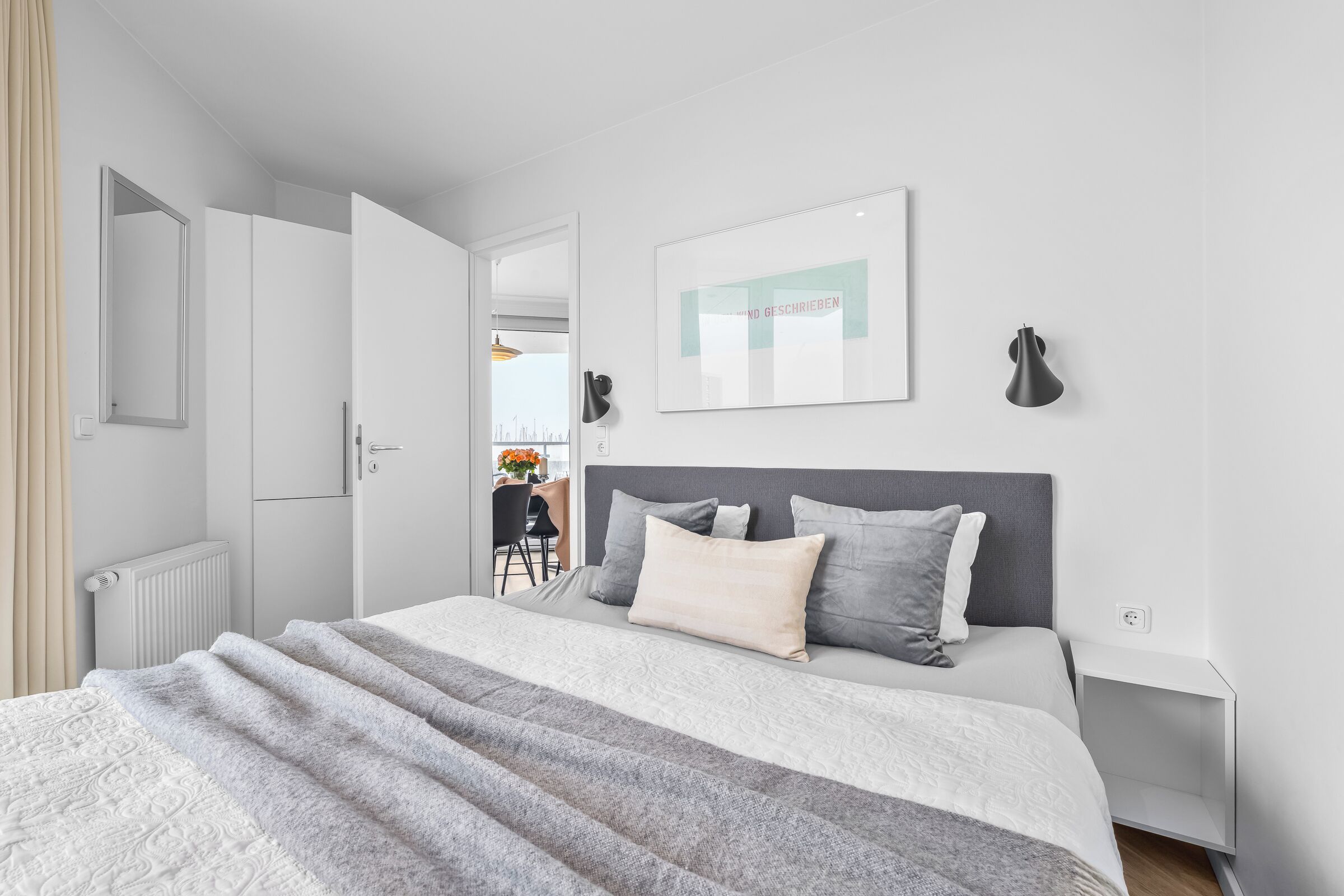 Ein modernes Schlafzimmer mit Bett, Nachttischen, Heizkörper, Spiegel und einem gerahmten Bild an der Wand.