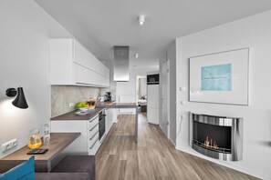 Una cocina moderna con una isla central, una zona de comedor con una silla azul y una chimenea.