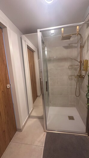 Une douche fermée par des parois en verre, dotée d’un pommeau de douche à main et d’un robinet fixé au mur.