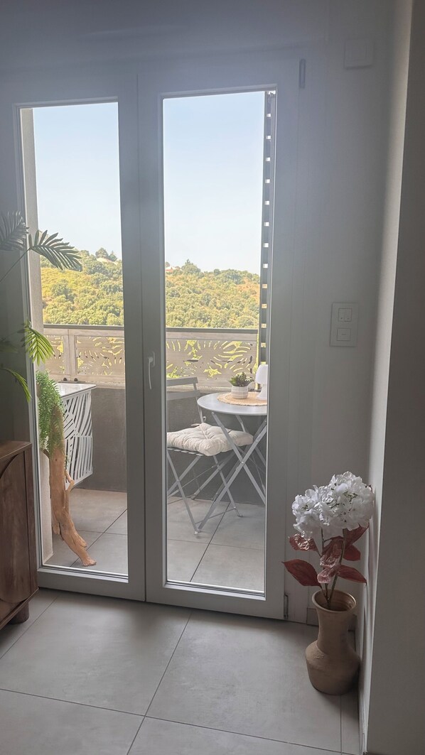 A balcony with a table, chairs, a potted plant, and a view of a green landscape. - Charming 1-bedroom apartment with mountain views, 10 minutes from Tahiti Beach and Capitello (Sarrola carcopino)