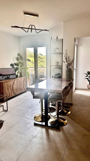 Un espace repas moderne avec une table à plateau en verre, des tabourets de bar et une vue sur l’extérieur.