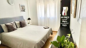 Quarto com cama, mesa de cabeceira, espelho, planta em vaso e um quadro na parede.