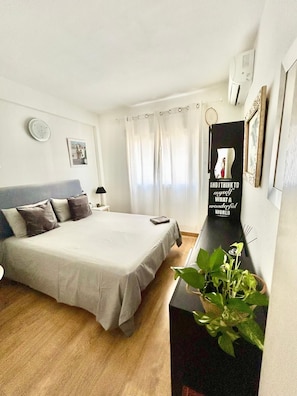 Une chambre à coucher comprenant un lit, une table de chevet, un miroir, une plante en pot et un tableau accroché au mur.