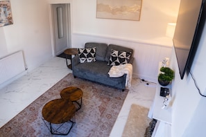 A living room with a sofa, two armchairs, a coffee table, a rug, a side table, a lamp, a plant, and a fireplace. - Stylish 2 Bedroom With Free Parking (Manchester)