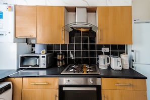 A compact kitchen with a microwave, toaster, kettle, and a stove. - Stylish 2 Bedroom With Free Parking (Manchester)