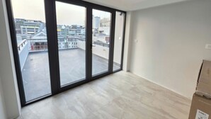 Ein Zimmer mit großen Fenstern, Fliesenboden und einem sichtbaren Balkon.