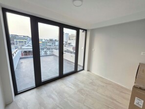 Une pièce dotée de grandes fenêtres, d’un sol carrelé et d’un balcon apparent.