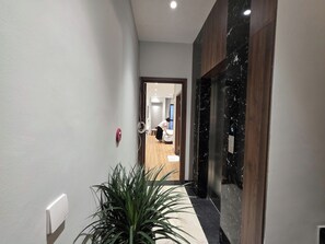 A hallway with a potted plant, a fire alarm, and a digital elevator display.