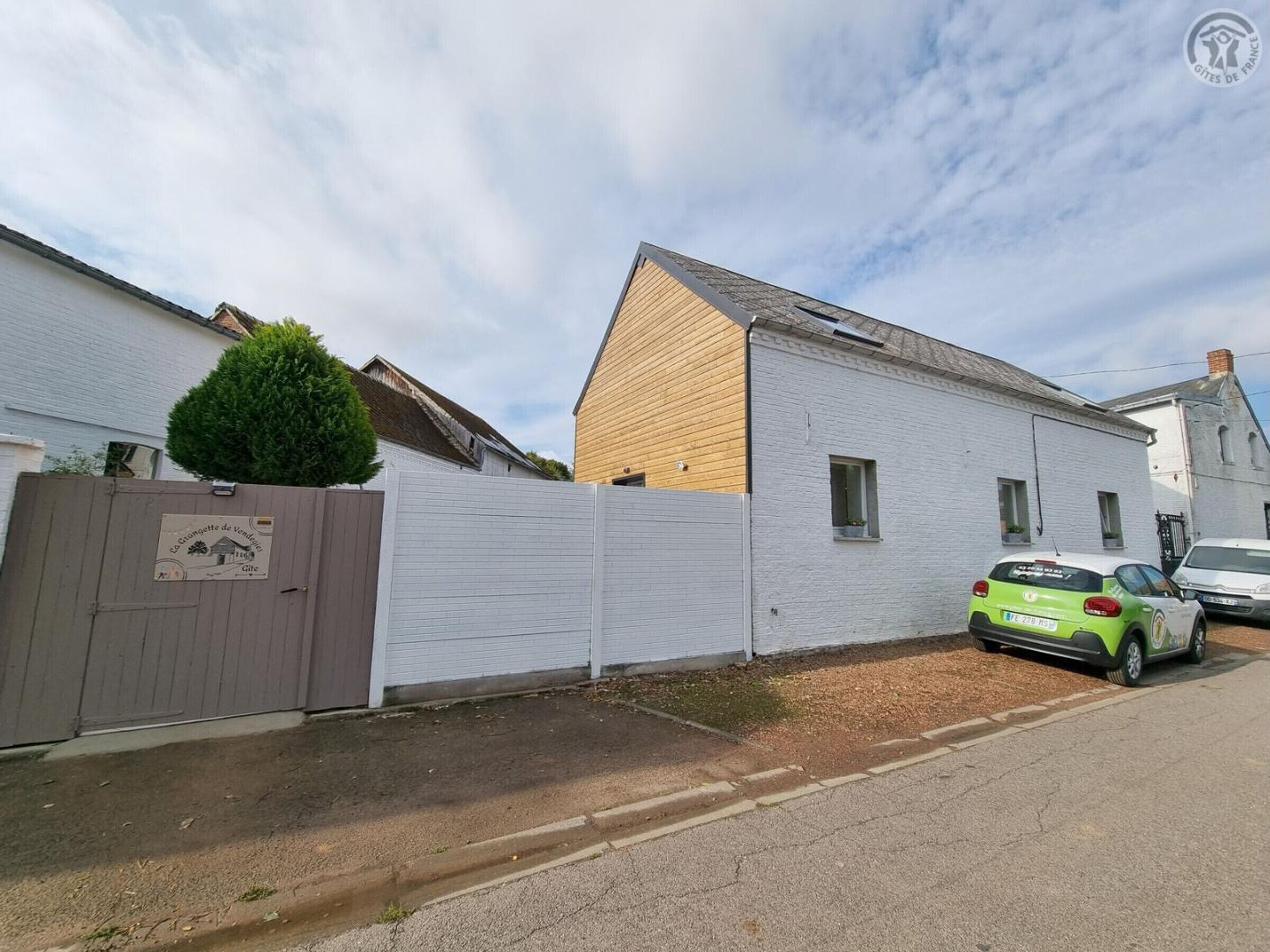 A residential street with a white house, a wooden fence, and a parked car.
