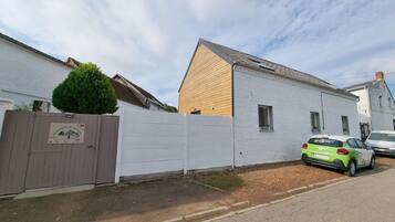 A residential street with a white house, a wooden fence, and a parked car.
