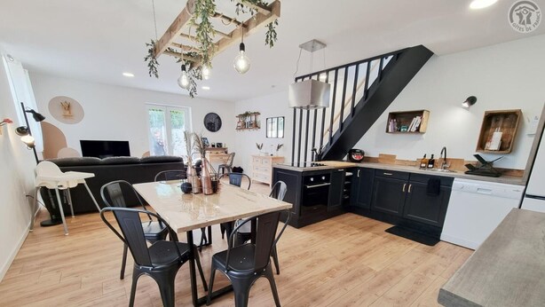A modern kitchen with a dining area, wooden flooring, and a staircase.