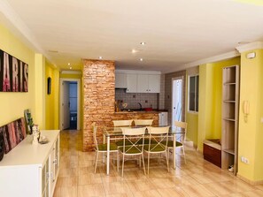 Una cocina moderna con una pared de acento de piedra, una zona de comedor con mesa y sillas de vidrio, y una pared amarilla con un teléfono.