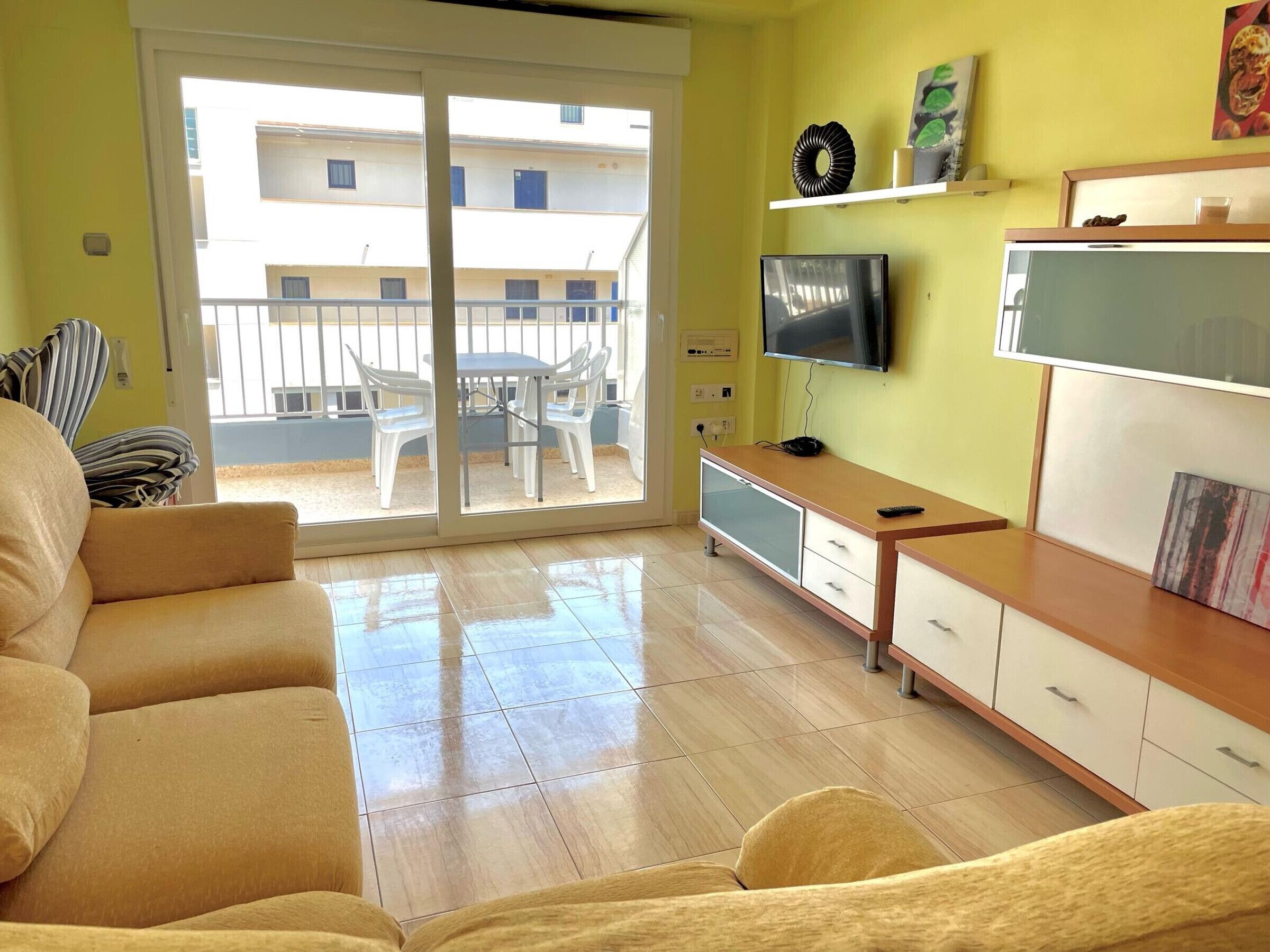 Un salon avec un canapé, un téléviseur et une porte-fenêtre coulissante donnant sur un balcon.