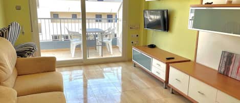 Una sala de estar con sofá, televisión y puerta corrediza de vidrio que da a un balcón.