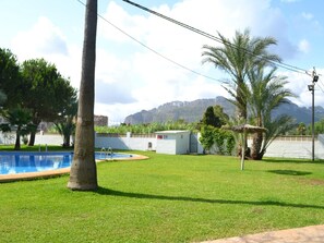 Ein Pool mit Rasenfläche, einer Palme und Bergen im Hintergrund.
