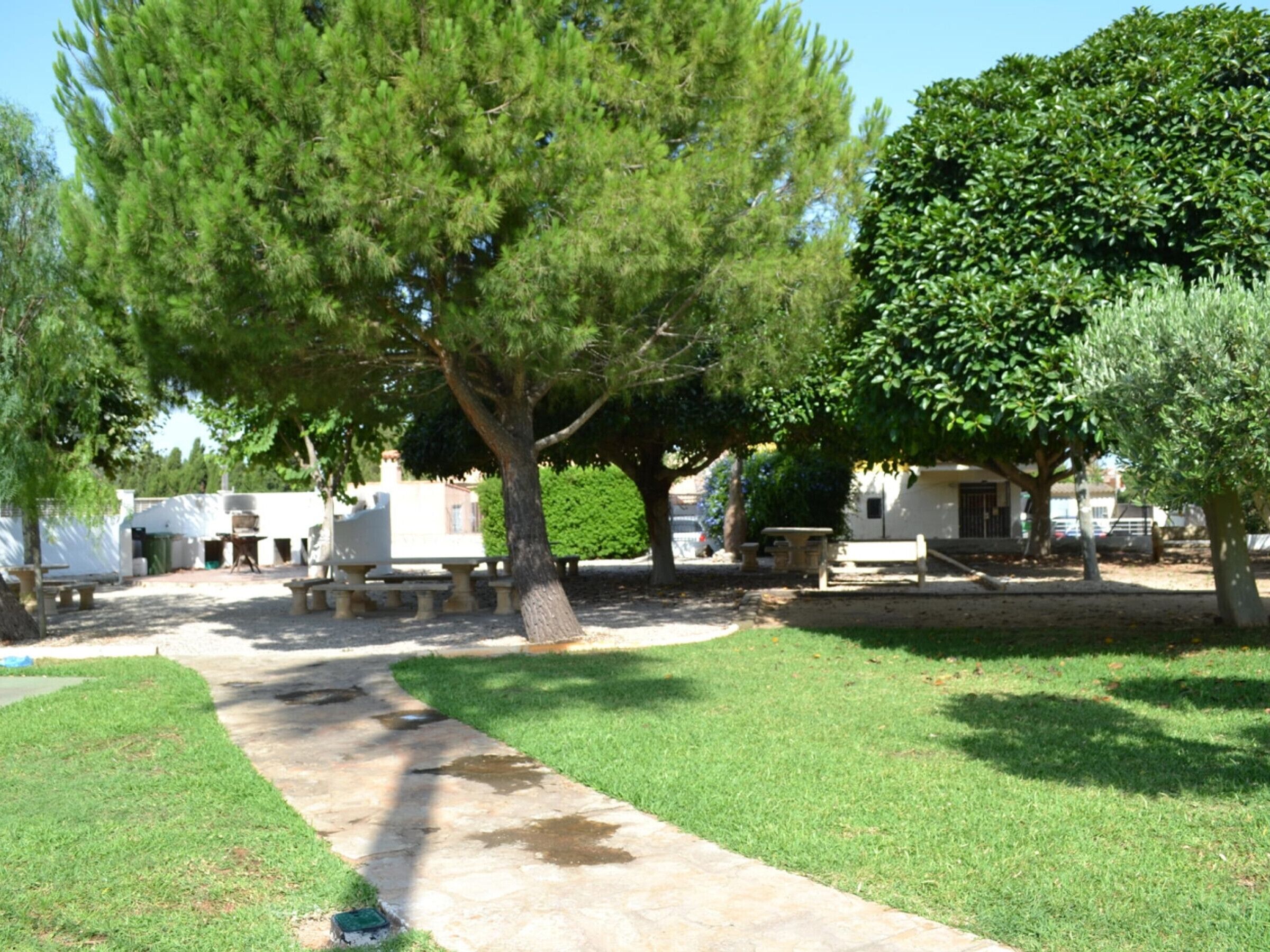 Un patio con un camino empedrado, mobiliario exterior y árboles.