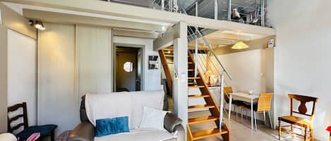 A modern living room with a sofa, a dining table, and a staircase leading to an upper level.