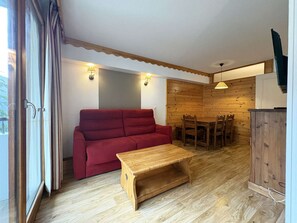 A room with a red sofa, wooden dining table, and chairs, wooden flooring, and a wooden wall panel. - Comfortable apartment - 6 guests (Les Orres)