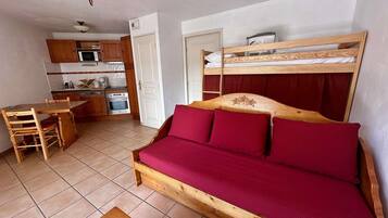 Une pièce compacte comprenant un lit superposé, une table à manger en bois, un coin cuisine avec un four à micro-ondes et un luminaire fixé au plafond.