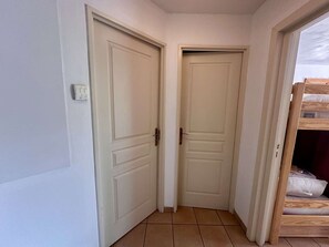 Ein Korridor mit zwei geschlossenen Türen, einem Lichtschalter an der Wand und einem hölzernen Etagenbett in der Ecke.