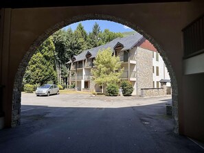 Un edificio de varios pisos con fachada de piedra, un estacionamiento y un coche estacionado frente a él.