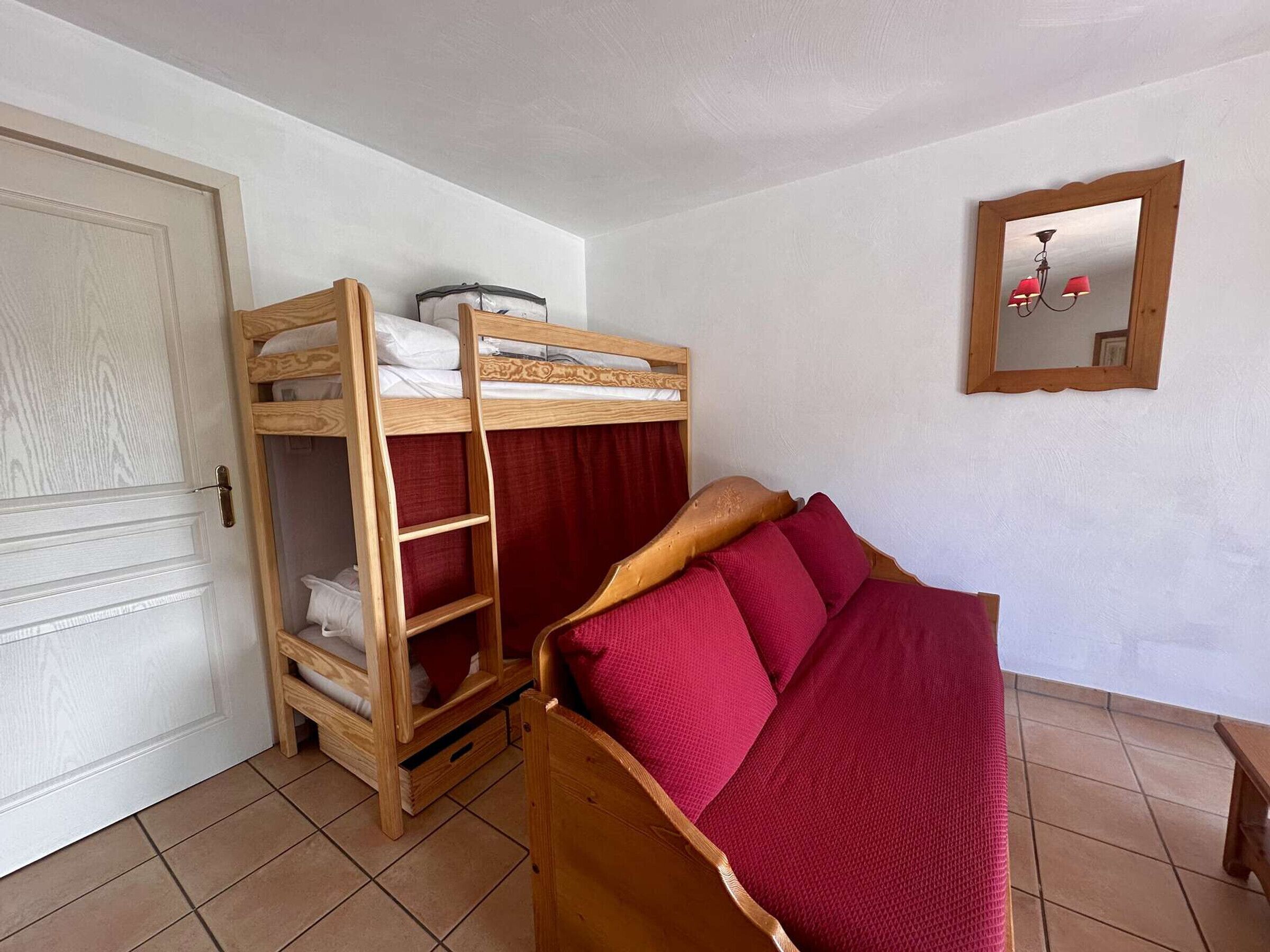 Une chambre avec un lit superposé, une armoire en bois, un miroir et un sol carrelé.