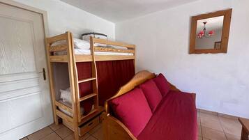 Une chambre avec un lit superposé, une armoire en bois, un miroir et un sol carrelé.