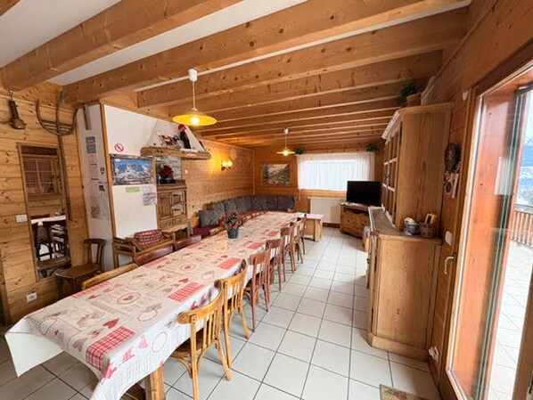 Et interiør af en træhytte med et spisebord, stole, en sofa, et fjernsyn og et køkkenområde.