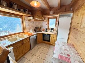 Eine kompakte Küche mit Holzschränken, einem Geschirrspüler, einem Kühlschrank und einem Fenster mit Blick ins Freie.