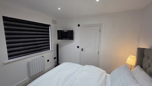 A bedroom with a bed, a TV mounted on the wall, a door, and a window with blinds.