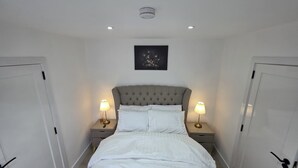 A bedroom with a bed, two bedside tables with lamps, a ceiling light, and a framed picture on the wall.