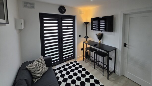 A modern living room with a sofa, a checkered rug, a dining area with a table and chairs, a mounted TV, and a door.