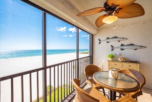 Un balcon avec vue sur la plage, des meubles en osier, un ventilateur de plafond et des poissons décoratifs accrochés au mur.