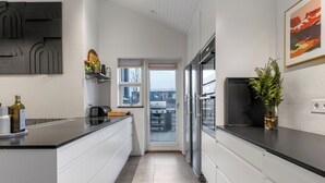 Una cucina moderna con mobili bianchi, un piano di lavoro nero, un frigorifero in acciaio inossidabile e una finestra vista sulla città.