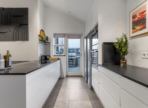 Eine moderne Küche mit weißen Schränken, einer schwarzen Arbeitsplatte, einem Edelstahlkühlschrank und einem Fenster mit Blick auf die Stadt.