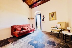 A room with a red sofa, a chair, a table with a lamp, a wooden ceiling, and a door leading outside. - GuestHost - Petra Pece Panoramic Apartment (Ragusa)