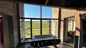 Uma mesa de futebol em uma sala com grandes janelas, paredes de tijolo e lareira de pedra.