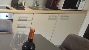 A kitchen with a microwave, sink, and cabinets. There is a bottle of wine and two glasses on the counter. - Sunny Pržno Escape Near Beaches with Pool & Indoor Garage (Pržno)