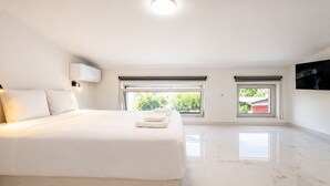 Quarto de hotel moderno com uma cama grande, duas janelas, uma TV de tela plana e uma luminária no teto.
