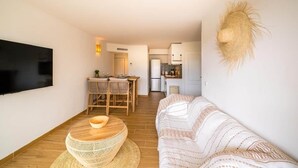 Ein Wohnzimmer mit Sofa, Fernseher, Essbereich mit Stühlen und einer Küche im Hintergrund.