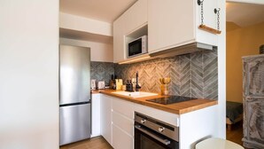 Eine kompakte Küche mit weißen Schränken, einer Mikrowelle, einem Edelstahl-Kühlschrank und einer Küchenrückwand mit Fischgrätenmuster.