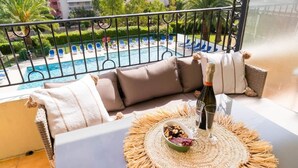 Ein Balkon mit Blick auf ein Schwimmbecken, ein Tisch mit Flasche und Gläsern sowie eine Schüssel mit Snacks.